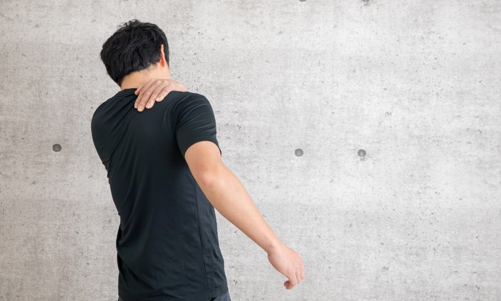 肩甲骨の内側が痛くて手を当てる男性